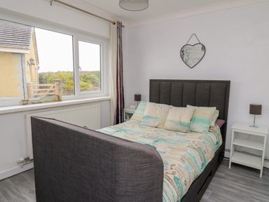 A bedroom with a grey upholstered bed and patterned bedding a window and a white bedside table at Ty Cwtch in Llangynin near St Clears