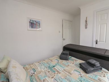 A bedroom with a bed covered in a patterned bedspread two folded towels on the bed a wall picture and two white doors at Ty Cwtch in Llangynin near St Clears