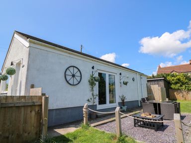 A white exterior wall of a house with hanging plants a glass door outdoor seating and firepit in a fenced garden area at Ty Cwtch in Llangynin near St Clears