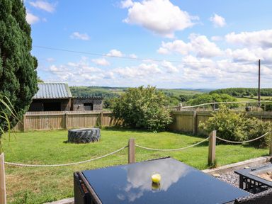 A garden with a table and chair a large tire a wooden shed and rolling hills in the background at Ty Cwtch in Llangynin near St Clears