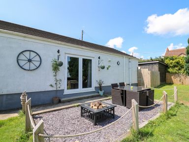 A backyard patio with a glass table and chairs a fire pit and potted plants at Ty Cwtch in Llangynin near St Clears