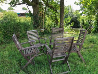 Five wooden chairs arranged in a circle on grass under trees with a small swing hanging from a tree limb at Ty Cwtch in Llangynin near St Clears