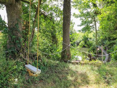 A garden area with a wooden swing hanging from a tree near a small pond at Ty Cwtch in Llangynin near St Clears