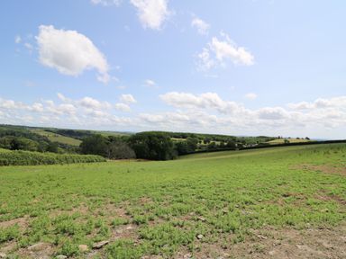 A grassy field with hills and trees under a partly cloudy sky at Ty Cwtch in Llangynin near St Clears