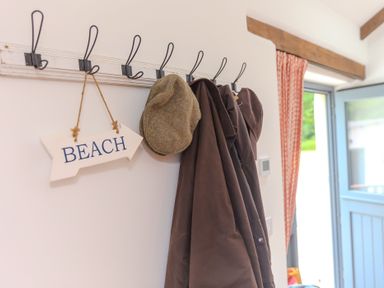 An entrance with a coat rack, a hat, and a beach sign at Carines Barns - Tre, Cubert