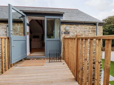 A wooden deck with a half open blue door leading to a room with a sofa at Carines Barns - Pol in Cubert