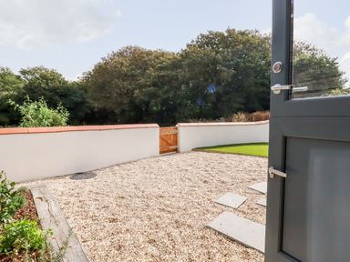 A gravel patio with stepping stones and a wooden gate leading to trees at Carines Barns - Pol in Cubert