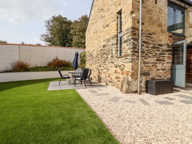 An outdoor patio area with a stone building and table with chairs on a tiled slab at Carines Barns - Pol in Cubert