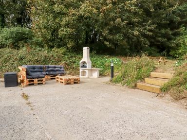 An outdoor seating area with wooden pallet furniture a barbecue and wooden steps leading to a picnic table at Carines Barns - Pol in Cubert