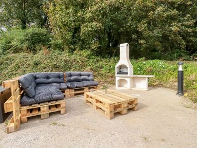An outdoor seating area with wooden pallet furniture cushions a stone barbecue and greenery Carines Barns - Pol Cubert