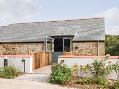 Exterior of a stone building with a slate roof a wooden ramp leading to a blue door and garden plants at Carines Barns Pol in Cubert