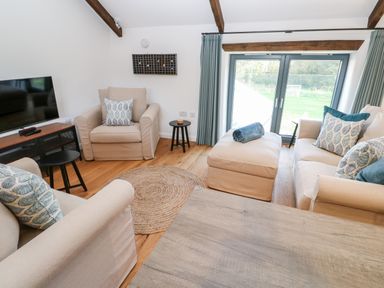 A living room with beige armchairs a sofa a round rug a wooden table and a TV at Carines Barns - Pol in Cubert