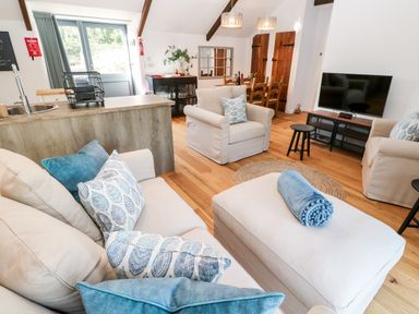 A living room with beige sofas and blue pillows a dining table and television at Carines Barns - Pol in Cubert