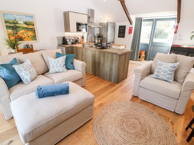 A living area with beige sofas and blue cushions near a kitchen island with wooden floors at Carines Barns - Pol in Cubert
