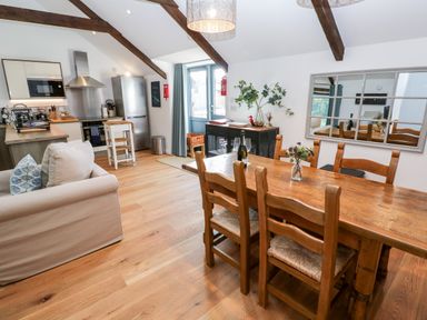 A kitchen and dining area with wooden table and chairs a couch and kitchen appliances at Carines Barns - Pol in Cubert