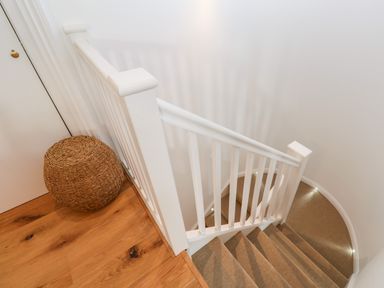 A staircase with white banisters and carpeted steps next to a wooden floor with a round woven basket at Carines Barns - Pol in Cubert