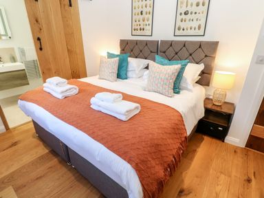 A bedroom with a double bed with orange throw and folded towels beside bedside tables with a lamp in Carines Barns Pol Cubert