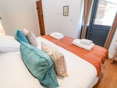 A bedroom with a bed made with white sheets and orange throw at Carines Barns - Pol in Cubert