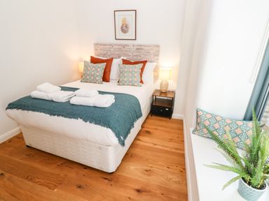 A bedroom with a bed with pillows and towels bedside tables with lamps and a plant on a window sill at Carines Barns - Pol in Cubert