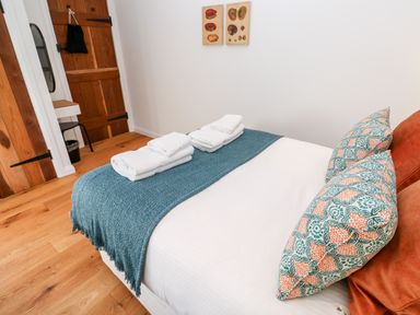 A bedroom with a bed with patterned pillows folded towels on a blue throw and wooden doors at Carines Barns - Pol in Cubert