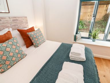 A bedroom with a bed with patterned and plain pillows towels on a blue blanket and a plant on the windowsill at Carines Barns - Pol in Cubert