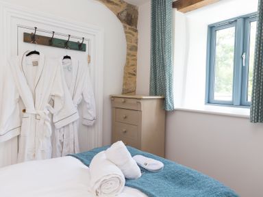 A bedroom with bathrobes hanging and a window at Carines Barns - Pen, Cubert