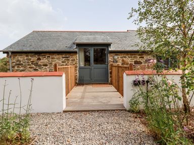 A stone house with a wooden ramp and double doors surrounded by a low wall and plants at Carines Barns - Par in Cubert