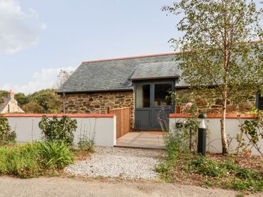 A stone house with a slate roof and a door leading to a small porch with white walls and plants around it at Carines Barns - Par in Cubert