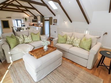 A living room with two beige sofas green cushions a wooden tray on an ottoman and exposed ceiling beams at Carines Barns - Par in Cubert