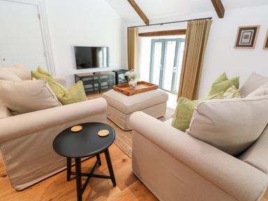 A living room with two beige sofas green pillows a black side table a wooden floor and a television at Carines Barns - Par in Cubert