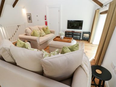 A living room with beige sofas and green cushions a wall mounted tv and a wooden tray on an ottoman at Carines Barns - Par in Cubert