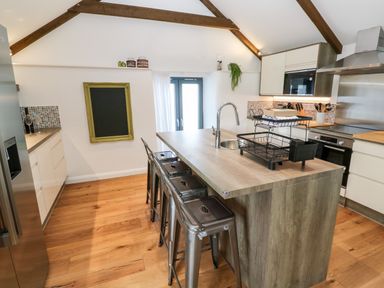 A kitchen with a wooden island and metal stools at Carines Barns - Par in Cubert