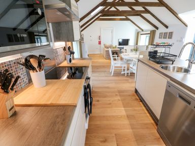 A kitchen with wooden countertops and utensils next to a dining area with a table and chairs under wooden ceiling beams at Carines Barns - Par in Cubert