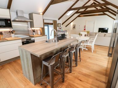 An open kitchen and living area with a kitchen island and bar stools at Carines Barns - Par in Cubert
