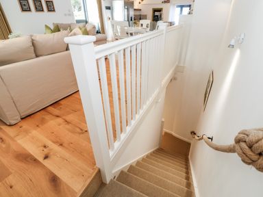 A staircase with a rope handrail leading to a living area with beige sofas and wooden flooring at Carines Barns - Par Cubert