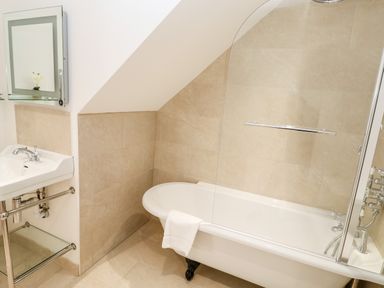 A bathroom with a bathtub a white towel a sink with a mirror and beige tiled walls at Carines Barns - Par in Cubert