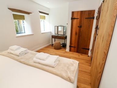 A bedroom with two windows a wooden door a dressing table and towels on a bed at Carines Barns - Par in Cubert