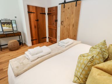 A bedroom with a bed with folded towels on it a dressing table with a mirror and wooden doors at Carines Barns - Par in Cubert