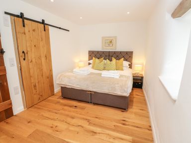 A bedroom with a double bed, bedside tables with lamps, a wooden sliding door, and a window at Carines Barns - Par in Cubert