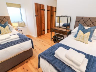 A bedroom with two single beds pillows and towels a wooden floor and a wooden dressing table at Carines Barns - Par Cubert
