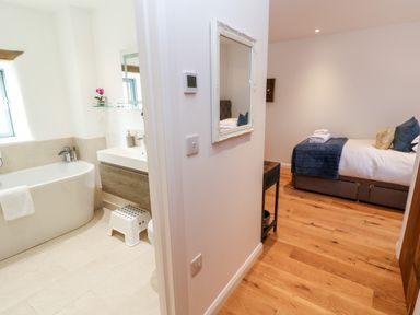 A bathroom with a bathtub and sink next to a bedroom with a bed and wooden floor at Carines Barns - Par in Cubert