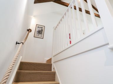 A carpeted staircase with a rope handrail a framed picture on the wall and wooden beams on the ceiling at Carines Barns - Par in Cubert