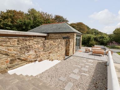 An outdoor patio area with stone steps gravel path wooden seating and a stone building at Carines Barns - Wesley Barn in Cubert