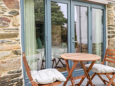 A wooden table with two padded wooden chairs outside blue French doors at Carines Barns - Wesley Barn in Cubert