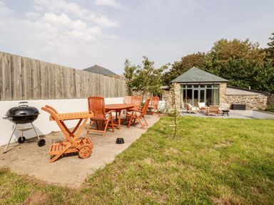 An outdoor area with a wooden dining table and chairs a barbecue grill and seating near a stone building at Carines Barns Wesley Barn in Cubert
