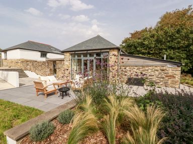 An outdoor patio with wooden chairs and a table near stone buildings with slate roofs at Carines Barns - Wesley Barn in Cubert