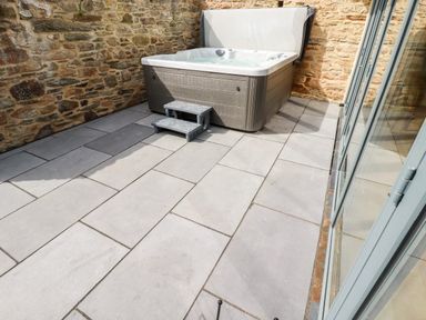 A hot tub with steps on a tiled patio next to a stone wall at Carines Barns - Wesley Barn in Cubert