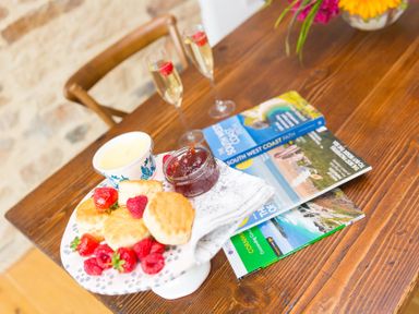 A table with scones, jam, strawberries, and magazines at Carines Barns - Wesley Barn in Cubert