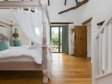 A bedroom with a four-poster bed and large doors to an outdoor area at Carines Barns - Wesley Barn in Cubert
