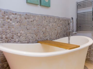 A bathroom with a bathtub and wooden bath tray at Carines Barns - Wesley Barn in Cubert